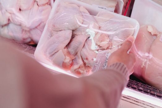 A shopper selects packaged chicken from a grocery store meat section.